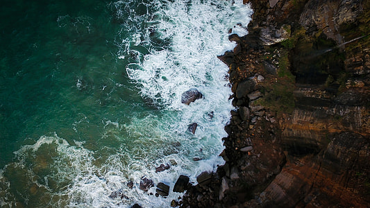 aerial view of body of water waves near rock formation thumbnail