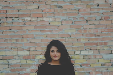 woman wears black top standing beside brown bricked wall thumbnail
