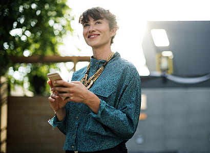 selective focus photography of woman holding iPhone standing near trees thumbnail