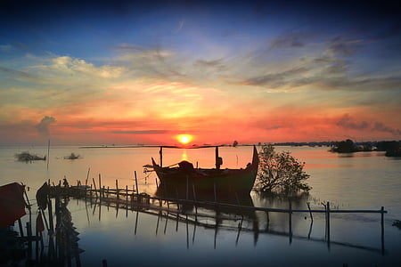 silhouette of boat on body of water at sunset thumbnail