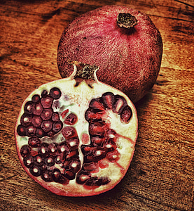 red sliced pomegranate on brown wooden surface thumbnail