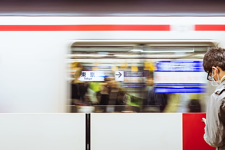 man standing in front of moving train while wearing white earbuds and using smartphone thumbnail