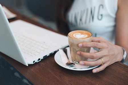 person holding glass cup with frappe beside white laptop computer thumbnail