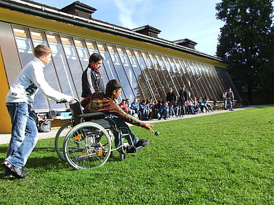 boy sitting on wheelchair throwing ball in green grass thumbnail