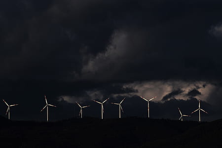 white windmills on black mountains under gray cloudy sky thumbnail