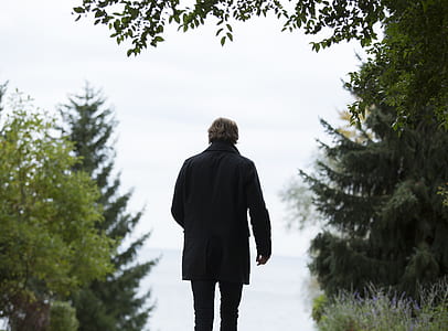 Shallow Focus Photography of Man Wearing Black Coat and Black Pants Standing Beside Green Trees thumbnail