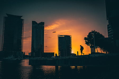 silhouette of man walking at dock with buildings during golden hour thumbnail