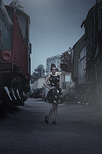 women's wearing black dress between trains during night time thumbnail