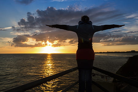 person opening arms while standing on corner of ship during golden hour thumbnail