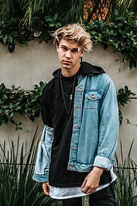 man wearing blue denim jacket standing behind plants thumbnail