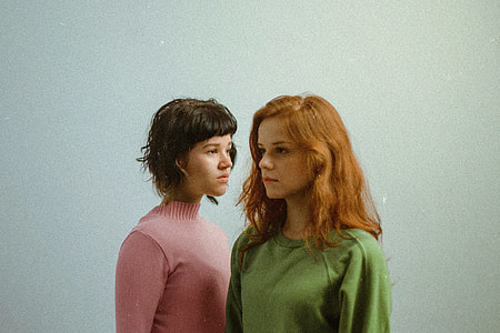 woman wearing pink turtle neck shirt while standing front of woman wearing green crew-neck shirt thumbnail