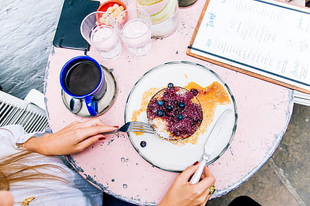 Woman Holding Spoon and Fork With Blackberries on Plate Beside Blue Ceramic Mug on White Wooden Table thumbnail