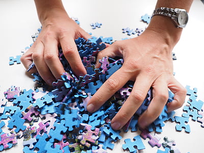 person grabbing bunch of blue and purple jigsaw puzzle pieces thumbnail