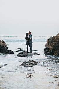 man and woman kissing each other standing on black rock formation during daytime thumbnail