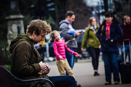 man wearing brown jacket sitting on black metal bench during daytime thumbnail