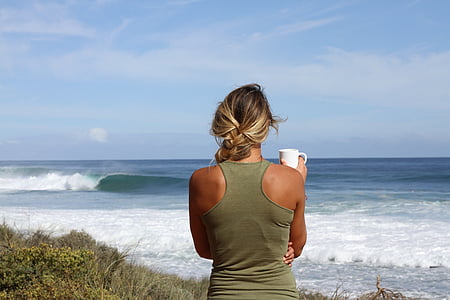 woman in green racer-back tank top holding white ceramic mug facing sea thumbnail