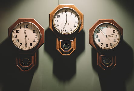 three brown pendulum analog clocks on gray wall thumbnail