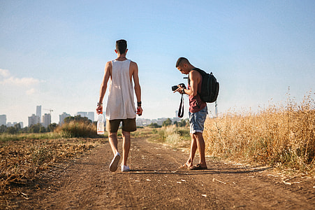 man wearing tank top standing beside man wearing brown tank top holding black DSLR camera thumbnail