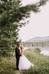 couple standing between trees and body of water while looking each other at daytime thumbnail