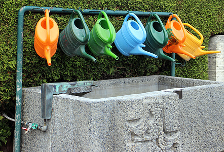 assorted-color watering cans hung on water pipeline thumbnail