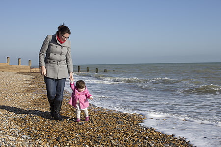 woman in grey double-breasted coat and toddler in pink jacket walking hand-in-hand at beach at daytime thumbnail