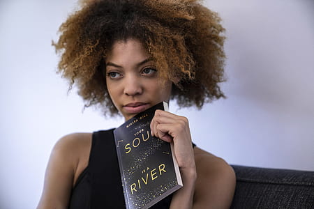 woman carrying book while sitting on black sofa thumbnail