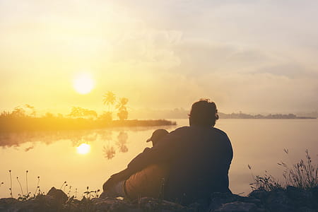 Two People On Grass Beside Body Of Water During Golden Hour thumbnail