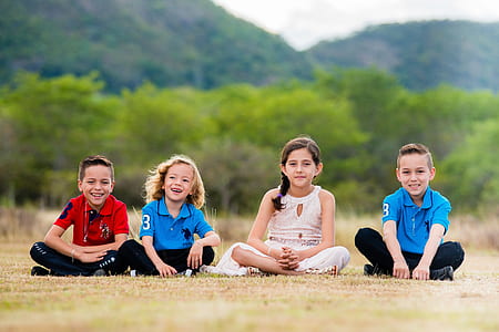 four boy and girl sitting on brown grass field thumbnail