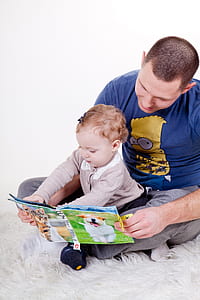 man and girl sitting on white fur textile while reading book thumbnail