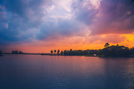 body of water near green trees during sunset thumbnail