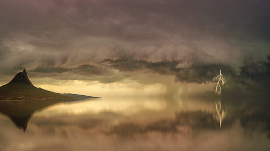 brown island surrounded by still body of water under clouds thumbnail