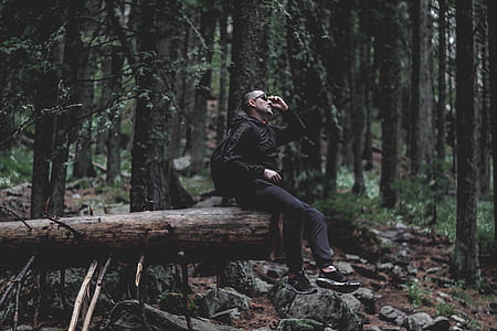 man wearing black jacket sitting on wood log while carrying backpack thumbnail
