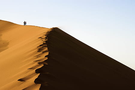 two person standing on sand dune under clear blue sky thumbnail