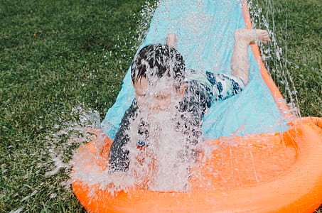 boy on orange and blue inflatable slide splashing water during daytime photo thumbnail