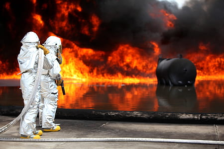 firefighters standing on concrete platform facing burning tank thumbnail