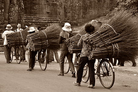 four people using bike while carrying stick brooms in sepia photography thumbnail