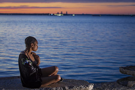 woman sitting on gray rock groynes in front of body of water thumbnail