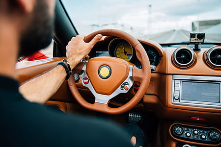 A bearded young man on driving a car with focus on dashboard and steering wheel thumbnail
