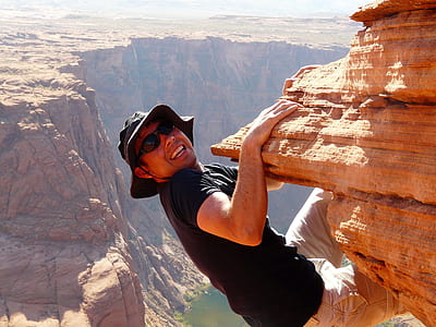 man in black t-shirt and black framed sunglasses climbing cliff thumbnail