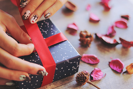 human's hand holding red ribbon while wrapping a blue box thumbnail