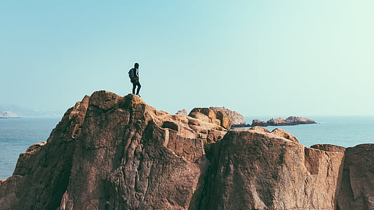 person on cliff near body of water thumbnail