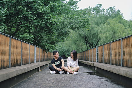 couple sitting on gray concrete floor between bench at daytime thumbnail