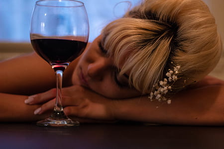 Woman With White Flower-accent Headdress Leaning Her Head on Table Beside Half-filled Wine Glass thumbnail