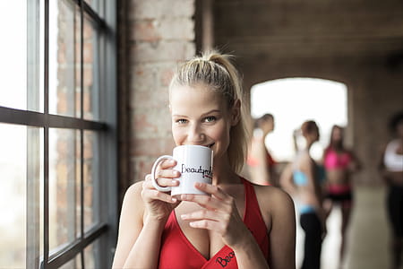 A young blonde woman wearing red sports bra holding coffee mug in her hands in the gym thumbnail