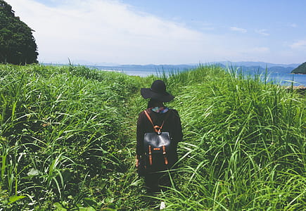 person in black hat standing in front grasses near body water thumbnail