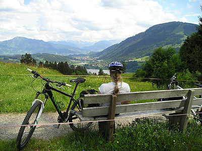 woman in white top sitting beside on bench beside bicycle thumbnail