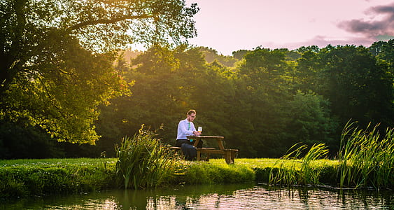 man sitting on picnic table near a lake thumbnail