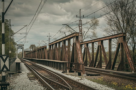 rusted brown metal bridge with train rails under cloudy sky during daytime thumbnail