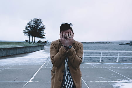 person wearing brown coat holding face standing during daytime thumbnail