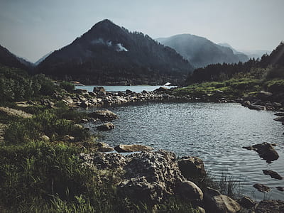 landscape photography of rocky body of water near green mountain thumbnail